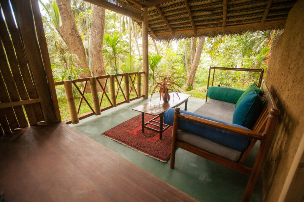 Bamboo hut veranda lounge with a daybed and palm garden views at Talalla Retreat, Sri Lanka