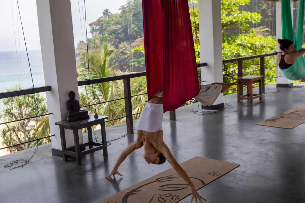 Aerial yoga in the open-air ocean-view shala at Talalla Retreat, Sri Lanka, with silk hammocks and a jungle backdrop.