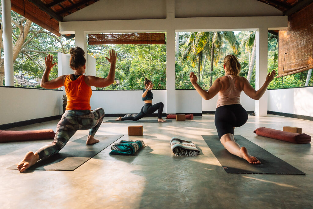 Women in low lunge with arms raised during a group yoga class at a yoga retreat in Sri Lanka, Talalla Retreat
