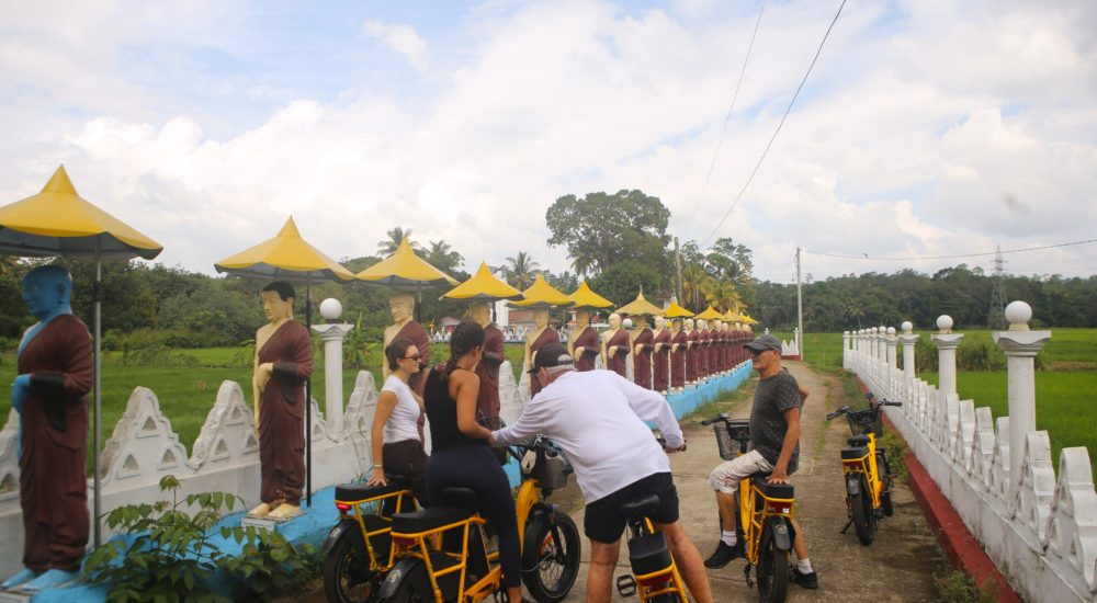 Guests on an e-bike temple tour past Buddhist statues and rice paddies near Talalla Retreat, Sri Lanka