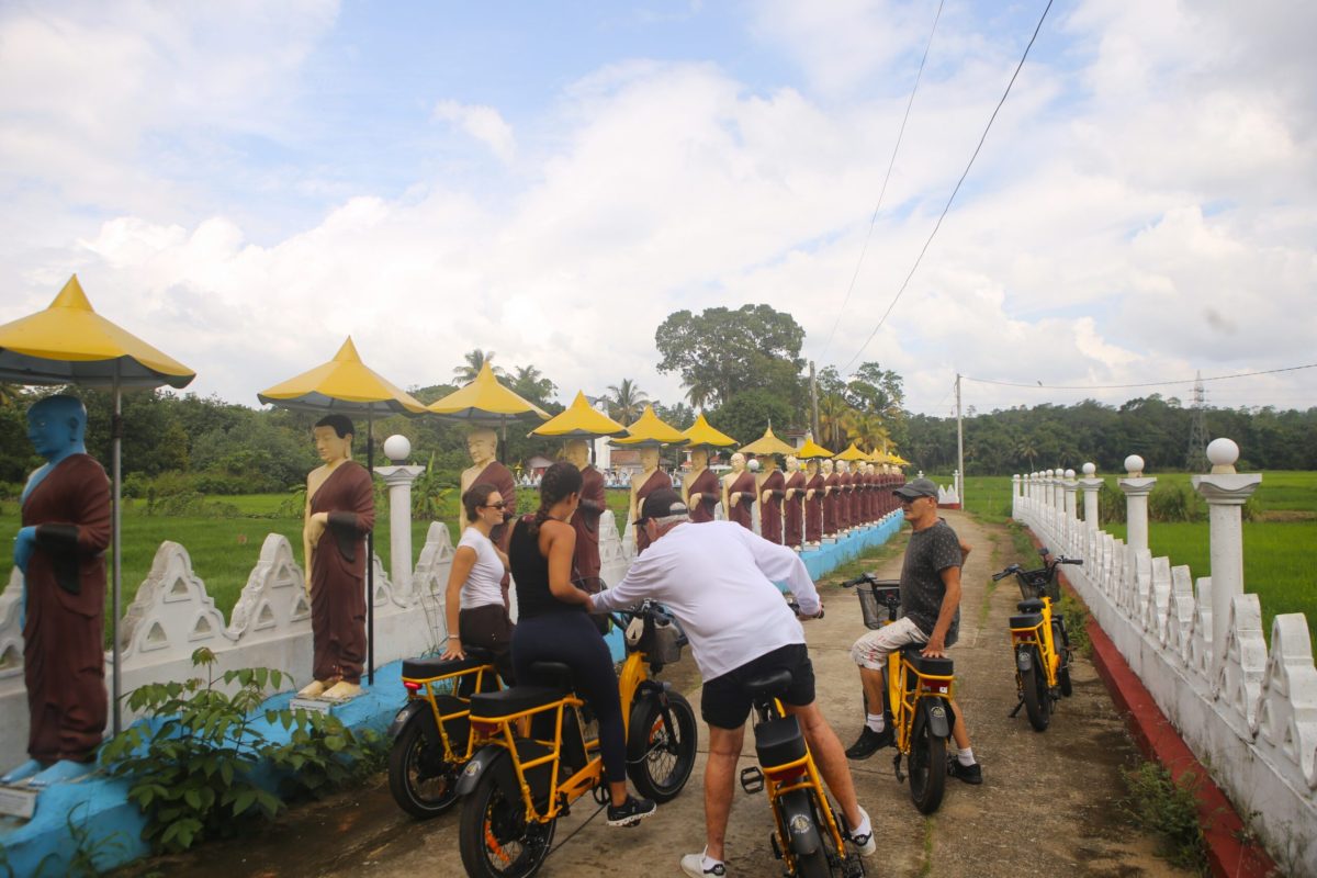 Guests on an e-bike temple tour past Buddhist statues and rice paddies near Talalla Retreat, Sri Lanka